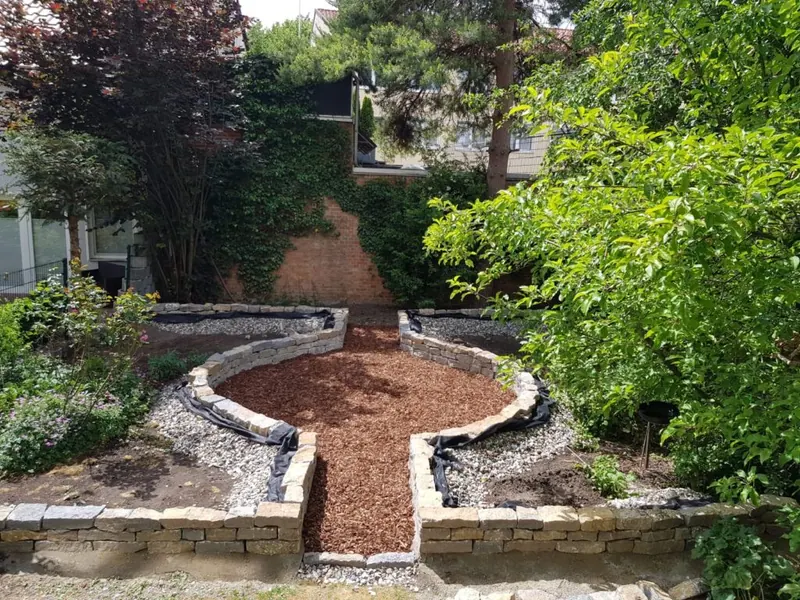 Naturnaher Garten mit Rindenmulchweg zwischen bepflanzten Natursteinmauern