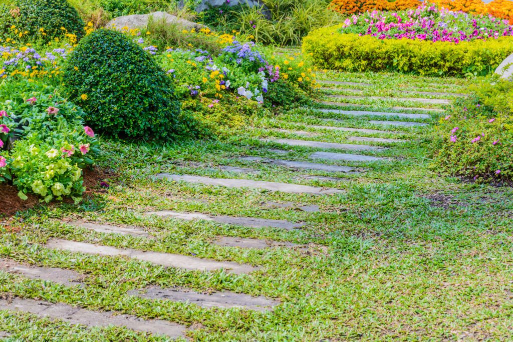 Gepflasterter Gartenweg aus Naturstein, umgeben von Blumenbeeten und Grünflächen in Salzhemmendorf